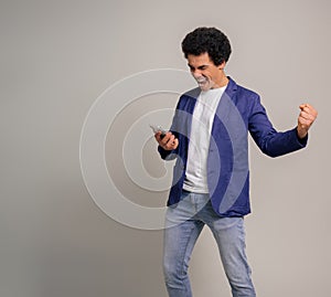 Carefree young man with afro hair and smart phone singing and playing air guitar on white background