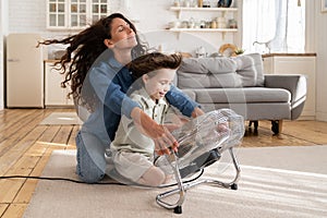 Carefree young mom or nanny have fun with boy son at home sitting together at big fan blowing air