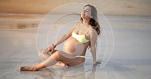 Carefree young pregnant woman relaxing on sandy beach in summer day.