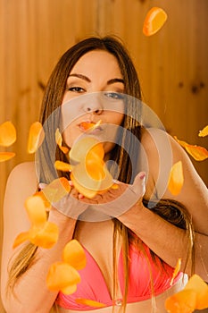 Carefree young woman blowing petals in sauna.