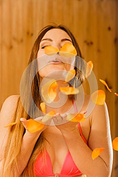 Carefree young woman blowing petals in sauna.