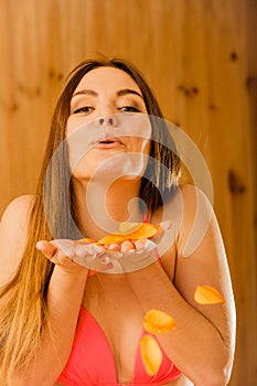 Carefree young woman blowing petals in sauna.