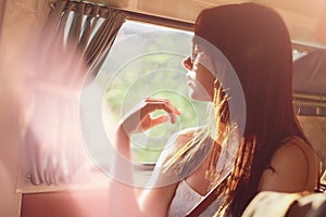 A carefree young woman in her camper van enjoying the warmth of the sun. Young woman on a road trip sitting in her van