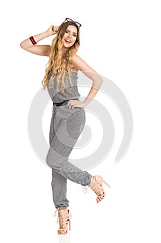 Carefree Young Woman In Jumpsuit Is Standing On One Leg And Smiling