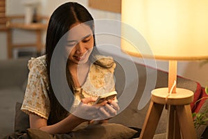 Carefree young woman relaxing on couch at home texting messaging, browsing wireless internet on smartphone