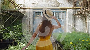 carefree young woman running in greenhouse in summertime, rear view in slow motion, enjoy life