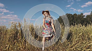 Carefree young woman walking through the field in a bright dress and a straw hat. slow motion