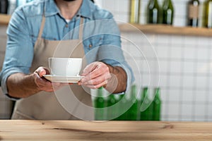 Careful attentive waiter putting a cup of coffee on the wooden table