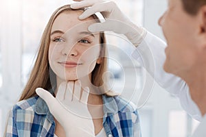 Careful dermatologist examining patient face at work