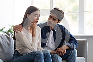 Careful european millennial man calms unhappy sad offended woman after quarrel in living room interior