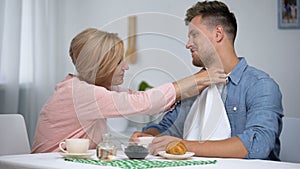 Careful mother putting napkin on son neck during having tea, overprotection