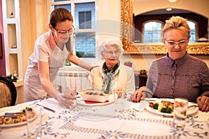 Careful nurse sets a table for dinner to patients at nursing home