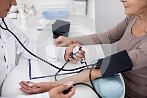 Careful practitioner sitting in front of the patient and measuring her pressure