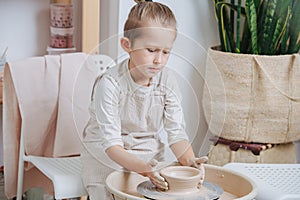 Careful serious boy shaping clay bowl on a pottery wheel at home workshop