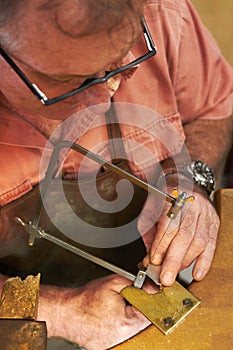 Carefully cutting out the shape - Jewelry manufacturing. Top view of a goldsmith about to saw into a piece of metal.