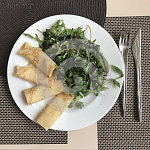 Carefully rolled crepes next to arugula on place mats