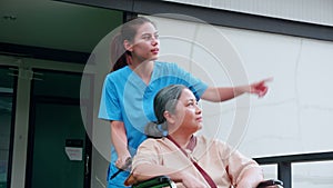 Caregiver asian woman walking while care elderly patient sitting on wheelchair in garden at hospital.