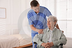 Caregiver assisting senior woman in wheelchair indoors. Home health care service