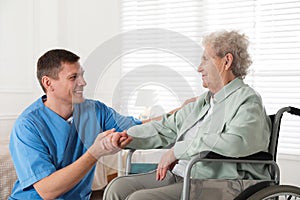 Caregiver assisting senior woman in wheelchair indoors. Home health care service