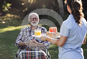 Caregiver carrying meal to senior man in wheelchair