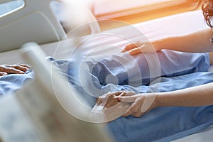 Caregiver and elderly senior patient (aged old adult person) holding hands in hospital bed or nursing hospice