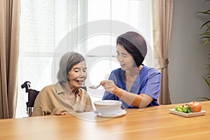 Caregiver feeding elderly asian woman with soup