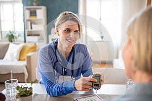 Caregiver or healthcare worker with senior woman patient, measuring blood glucose indoors.