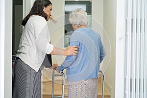 Caregiver help asian or elderly old woman walk with walker support up the stairs in home