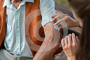 Caregiver helping senior diabetic man to apply continuous glucose monitor sensor on his arm.