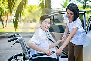 Caregiver helping senior handicapped asian woman from wheelchair get into car