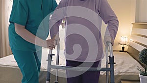 Caregiver helping senior woman getting up and walk with a walker