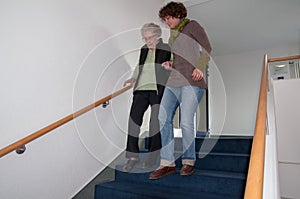 Caregiver helping senior woman walking down the stairs