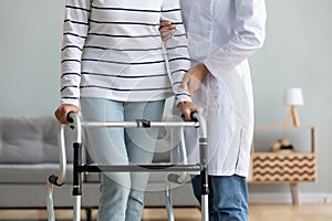 Caregiver helping to disabled aged female patient walk with walker