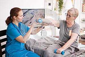 Caregiver helping using dumbbells for senior woman physiotherapy