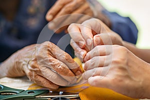 Caregiver holding thread the needle for elderly woman in the cloth crafts occupational therapy for Alzheimers or dementia