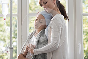 Caregiver hugging sick child with cancer wearing headscarf