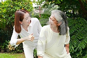 A caregiver or nurse does physical therapy for an elderly person in an outdoor garden.