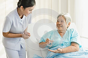 Caregiver nurse helping elderly woman taking medicine on the bed and check up after admit inpatient in hospital