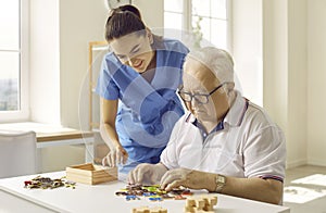 Caregiver or nurse in a retirement home helping a demented senior man with puzzles