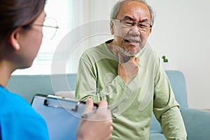 Caregiver nurse taking care of elderly grandfather sitting on sofa at home