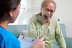 Caregiver nurse taking care of elderly grandfather sitting on sofa at home