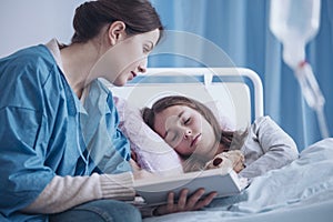 Caregiver reading a book to a sleepy sick girl in the clinic