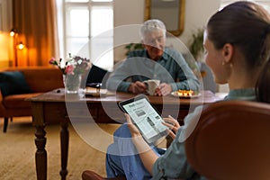 Caregiver reading online newspaper in digital tablet during taking care of senior man.