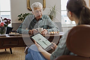 Caregiver reading online newspaper in digital tablet during taking care of senior man.
