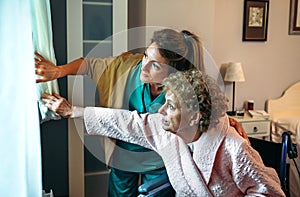 Caregiver showing the view through the window to elderly patient