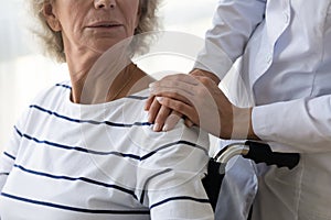Caregiver supporting disabled older woman, holding hands on shoulder