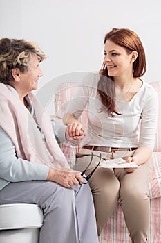 Caregiver talking with smiling senior woman while visit her at nursing house