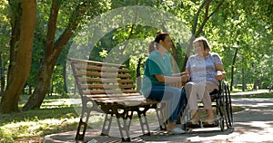 Caregiver talking to disabled senior woman in wheelchair outdoors