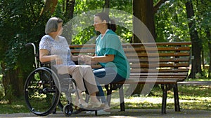 Caregiver talking to disabled senior woman in wheelchair outdoors