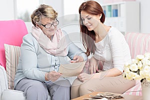 Caregiver watching photos while visiting happy elderly woman at home